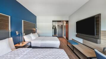 Una habitación de hotel con dos camas, televisión, escritorio y una banca.