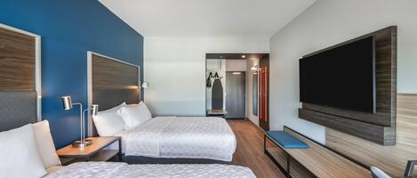 A hotel room with two beds, a flat-screen TV mounted on the wall, a desk, and a mirror.