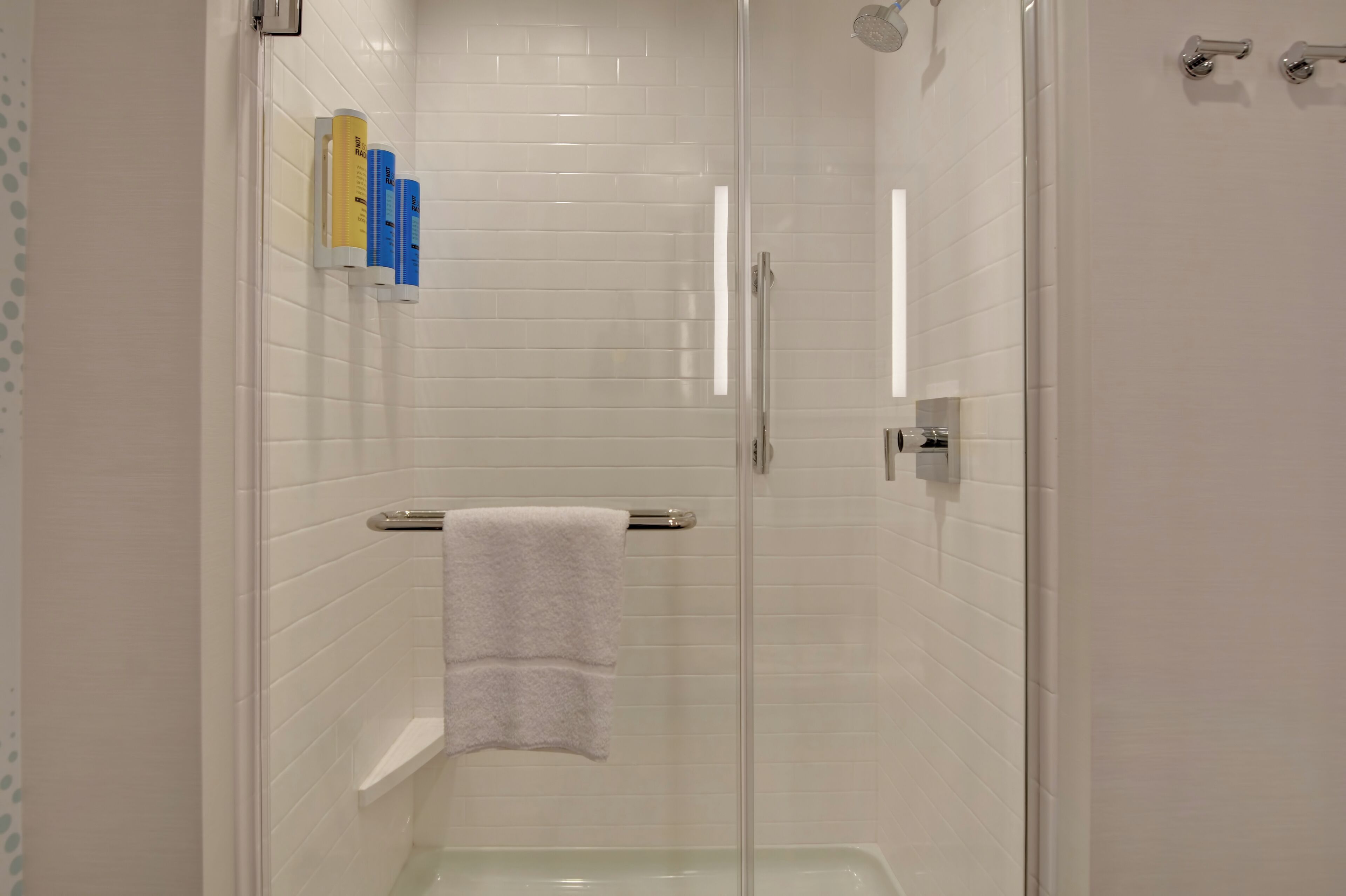 Une salle de bain moderne avec une douche à parois de verre, des murs recouverts de carreaux blancs et une serviette blanche posée sur un porte-serviettes.