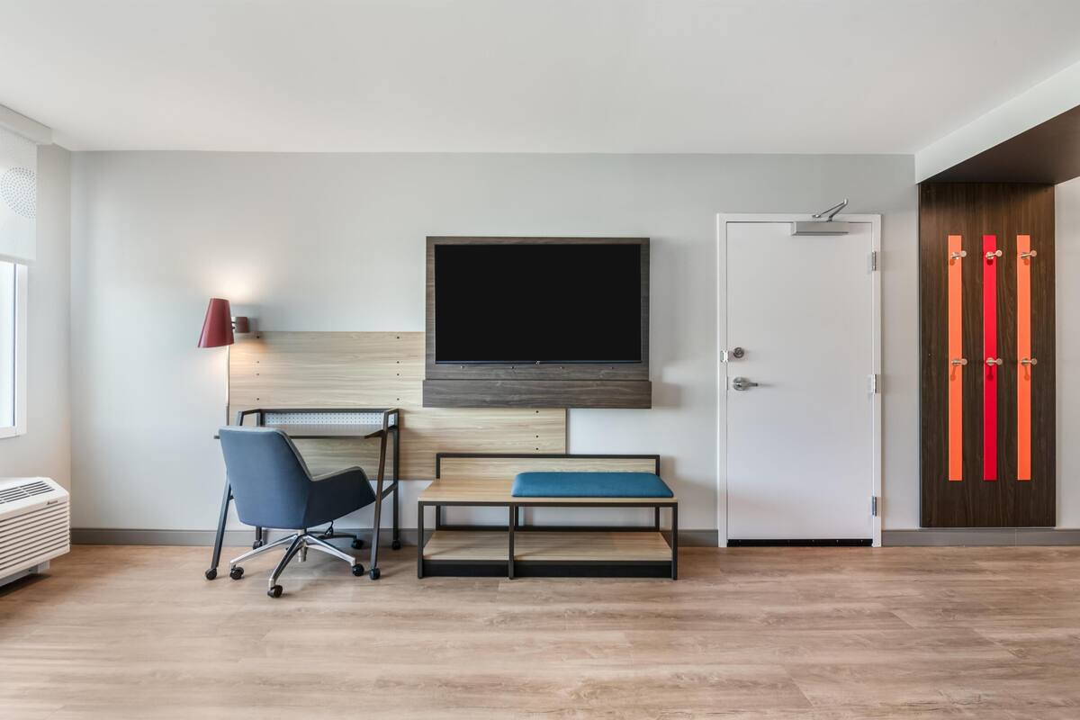 A modern room with a desk, chair, bench, TV, and wardrobe.