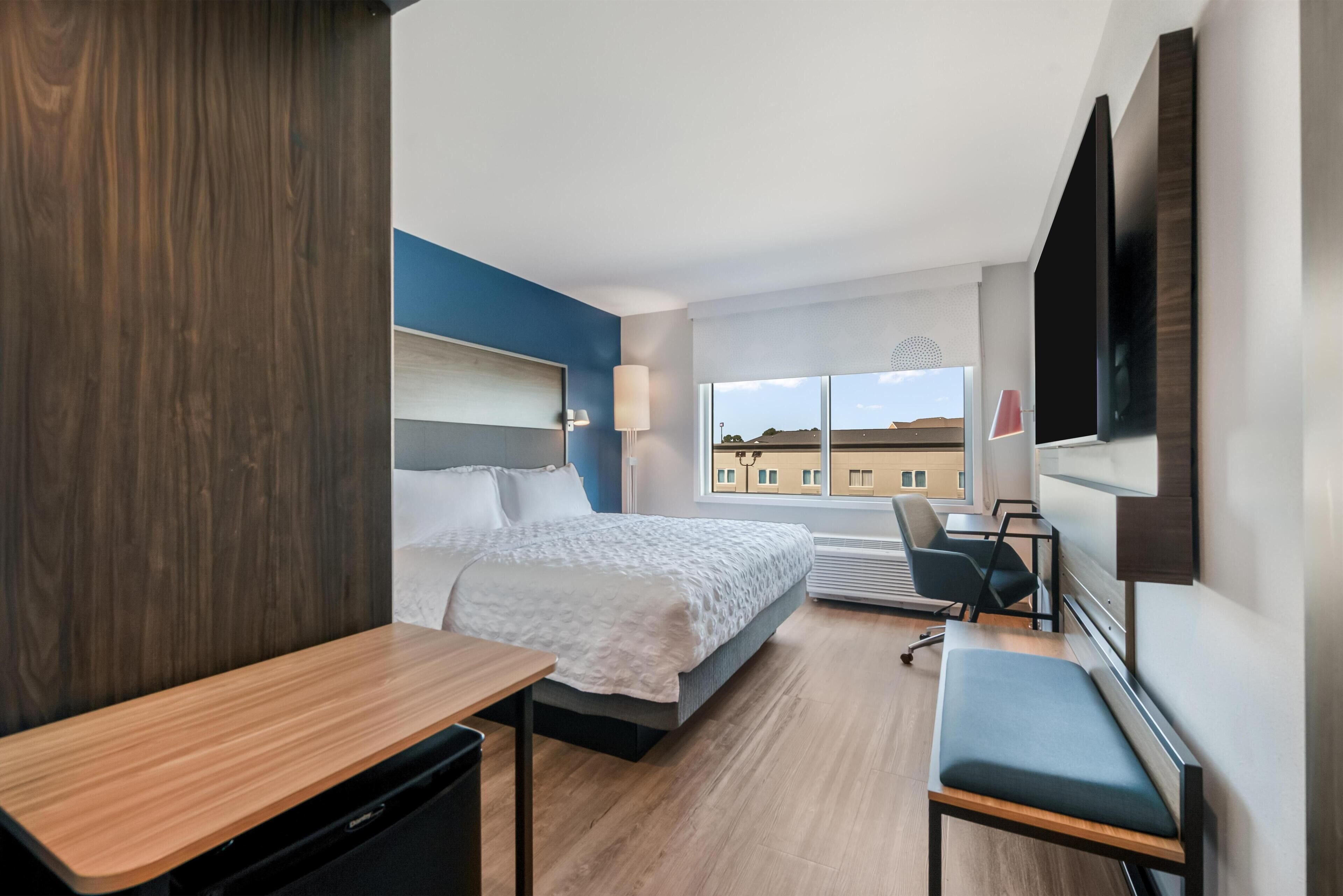 Une chambre d’hôtel équipée d’un lit, d’un bureau, d’une chaise, d’une télévision et de grandes fenêtres.
