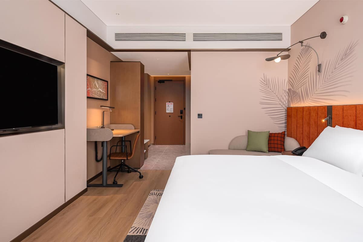 Een hotelkamer met een bed, een bureau, een stoel, een televisie en een wandlamp.