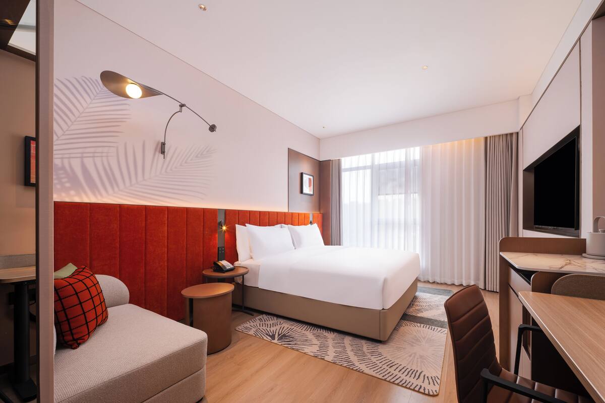 Een moderne hotelkamer met een groot bed, een bureau, een stoel, een klein tafeltje en een televisie.