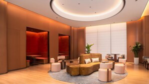 Un espace de détente moderne avec un canapé central, des tables rondes et un luminaire circulaire au plafond.