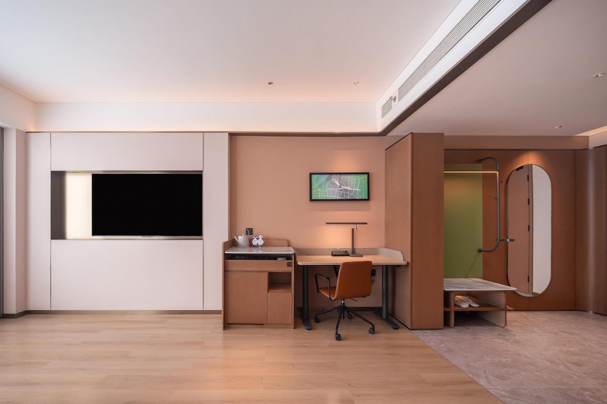 Een moderne slaapkamer met een flatscreen-tv, een bureau met stoel, een bed en een inloopkast.