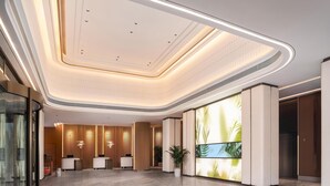 Un hall d’hôtel moderne doté d’un plafond incurvé, de comptoirs d’accueil, d’un grand écran numérique et d’une plante en pot.