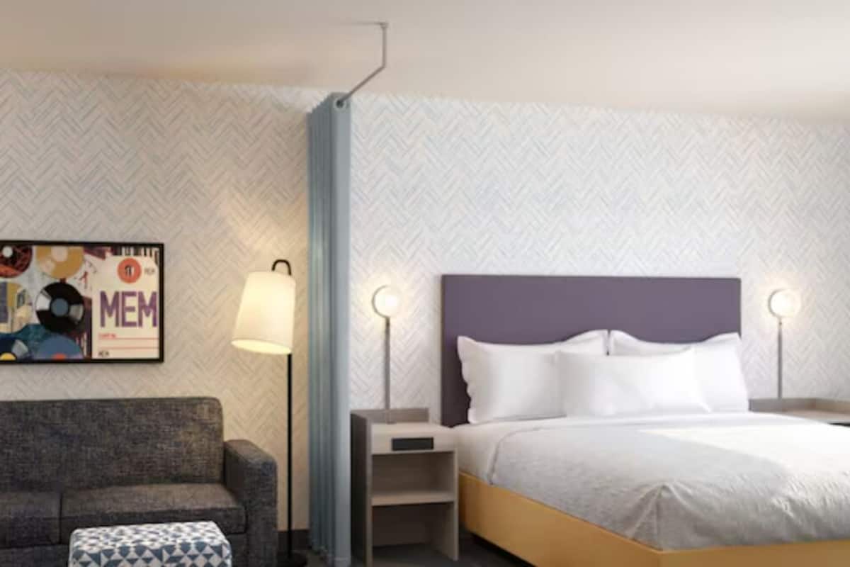 Una habitación de hotel con una cama, un sofá, una mesita auxiliar, una lámpara y una obra de arte en la pared.