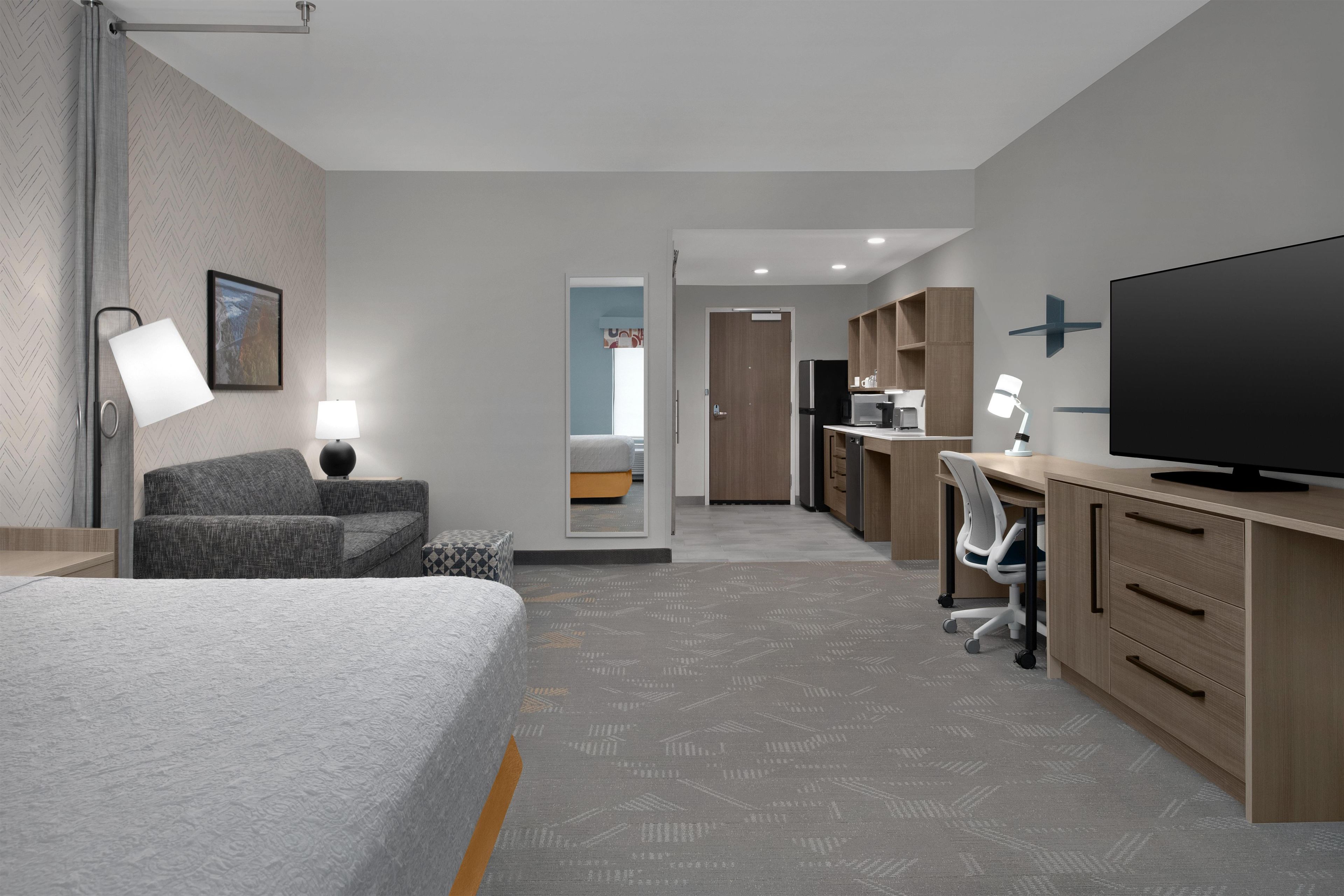 A hotel room with a bed, desk, chair, television, and a mirror.