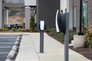 A parking area with electric vehicle charging stations, a covered outdoor seating area, and a building with a brick facade. - Home2 Suites By Hilton Ashburn, Va (Ashburn)