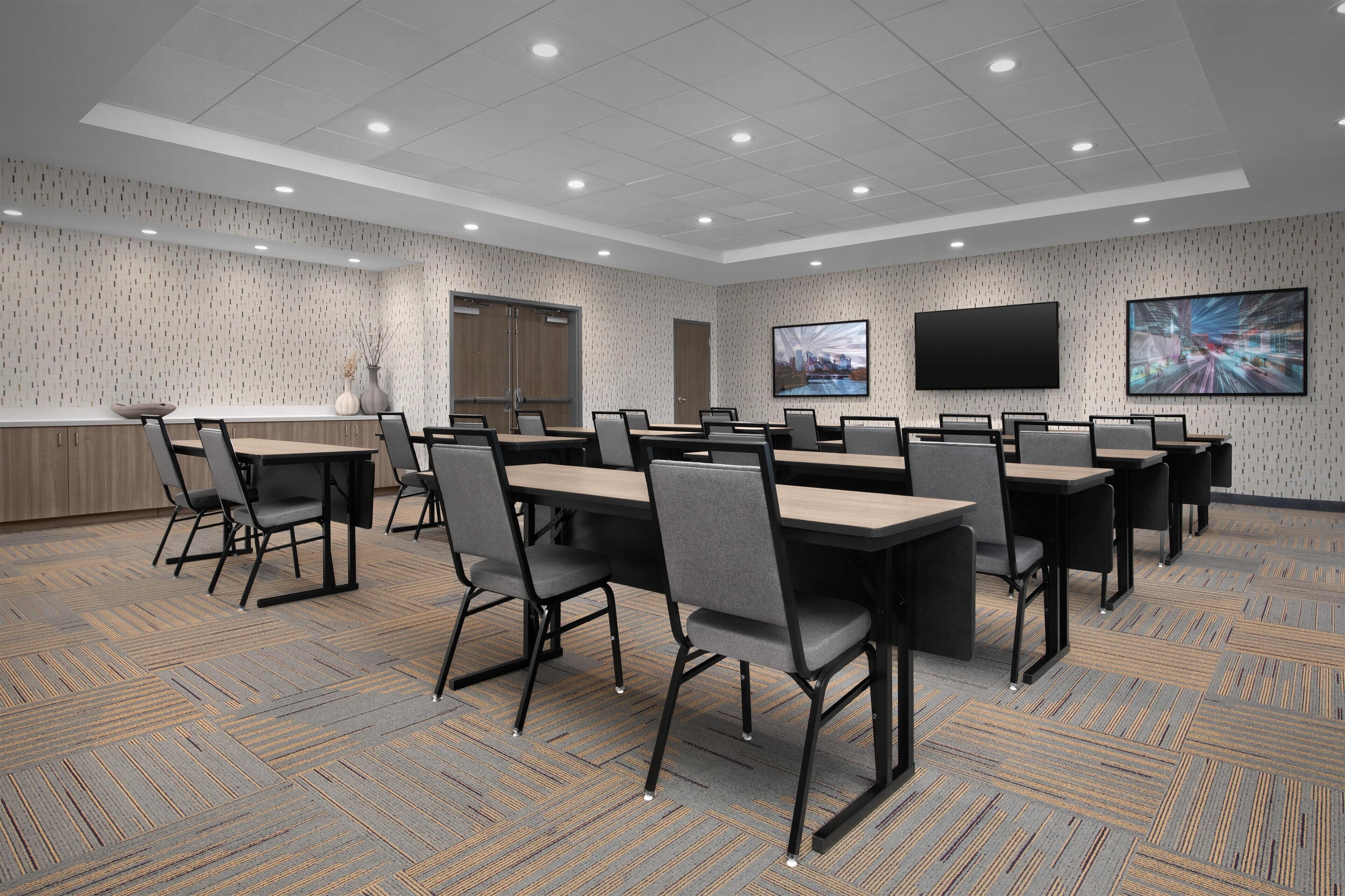 A conference room with multiple tables and chairs, a large screen, and a patterned carpet.
