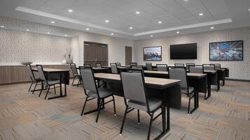 A conference room with multiple tables and chairs, a large screen, and a patterned carpet.