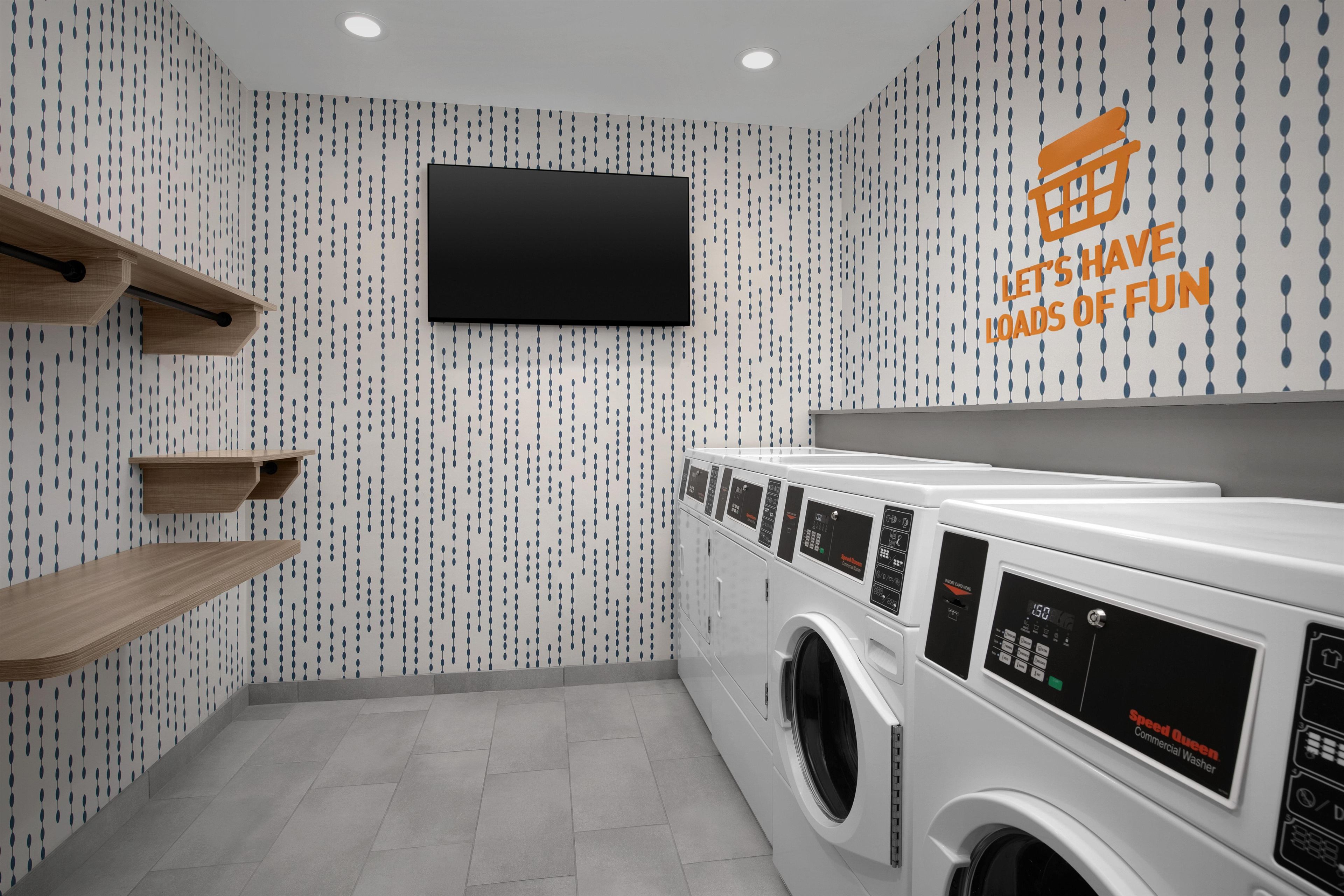 A laundry room with a wall-mounted TV, a washing machine, and wooden shelves.
