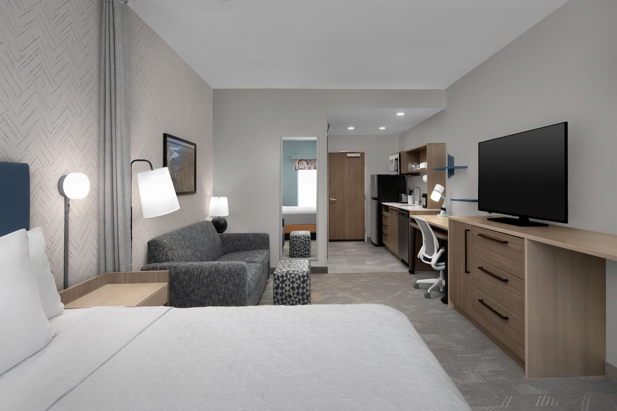 Habitación de hotel con cama, escritorio, televisión y baño visible a través de una puerta abierta.