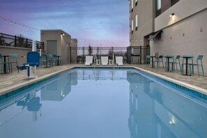 A swimming pool with lounge chairs and tables, surrounded by a fence and buildings. - Home2 Suites By Hilton Ashburn, Va (Ashburn)