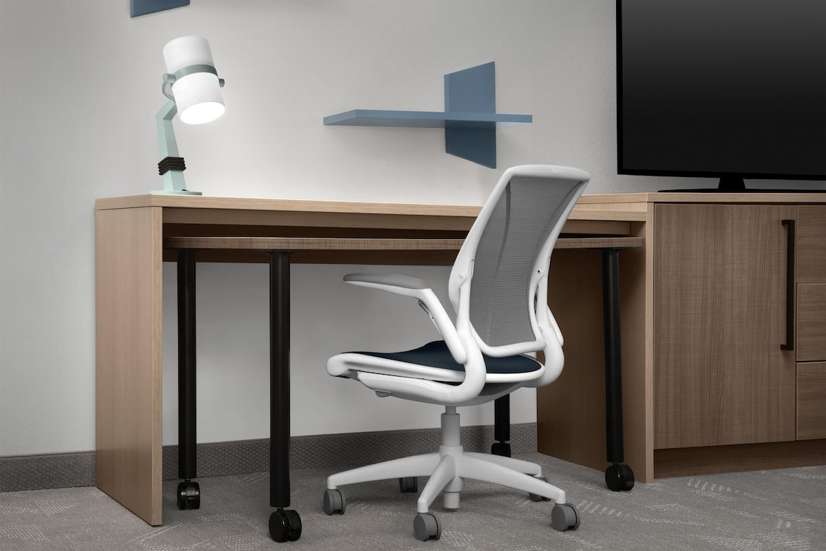 Un escritorio moderno con una silla giratoria, una lámpara de escritorio y un televisor.