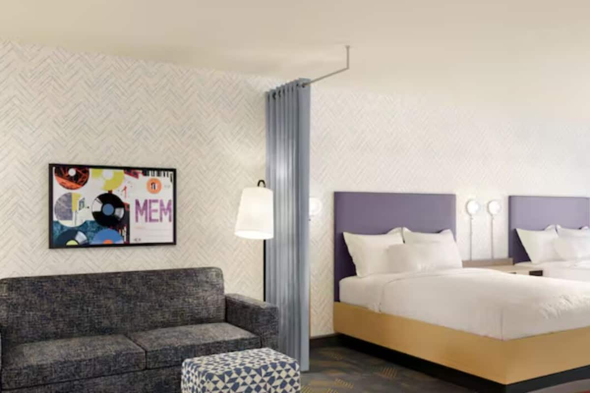 Una habitación de hotel con cama, sofá, mesita auxiliar y una obra de arte en la pared.