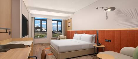 A modern hotel room with a large bed, a desk, a sofa, and a view of the outdoors.