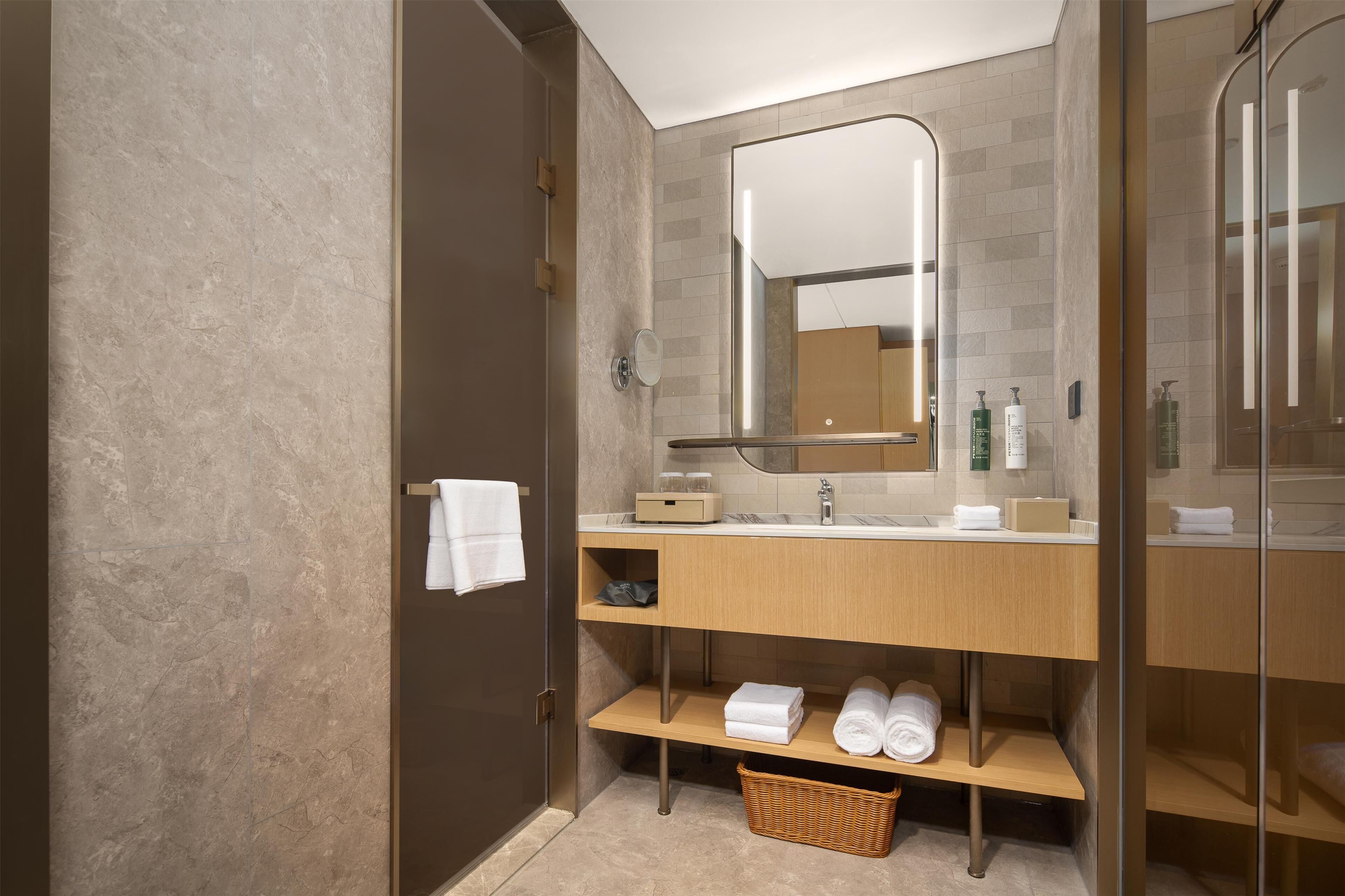 A modern bathroom with a wooden vanity, a large mirror, and a glass shower enclosure.