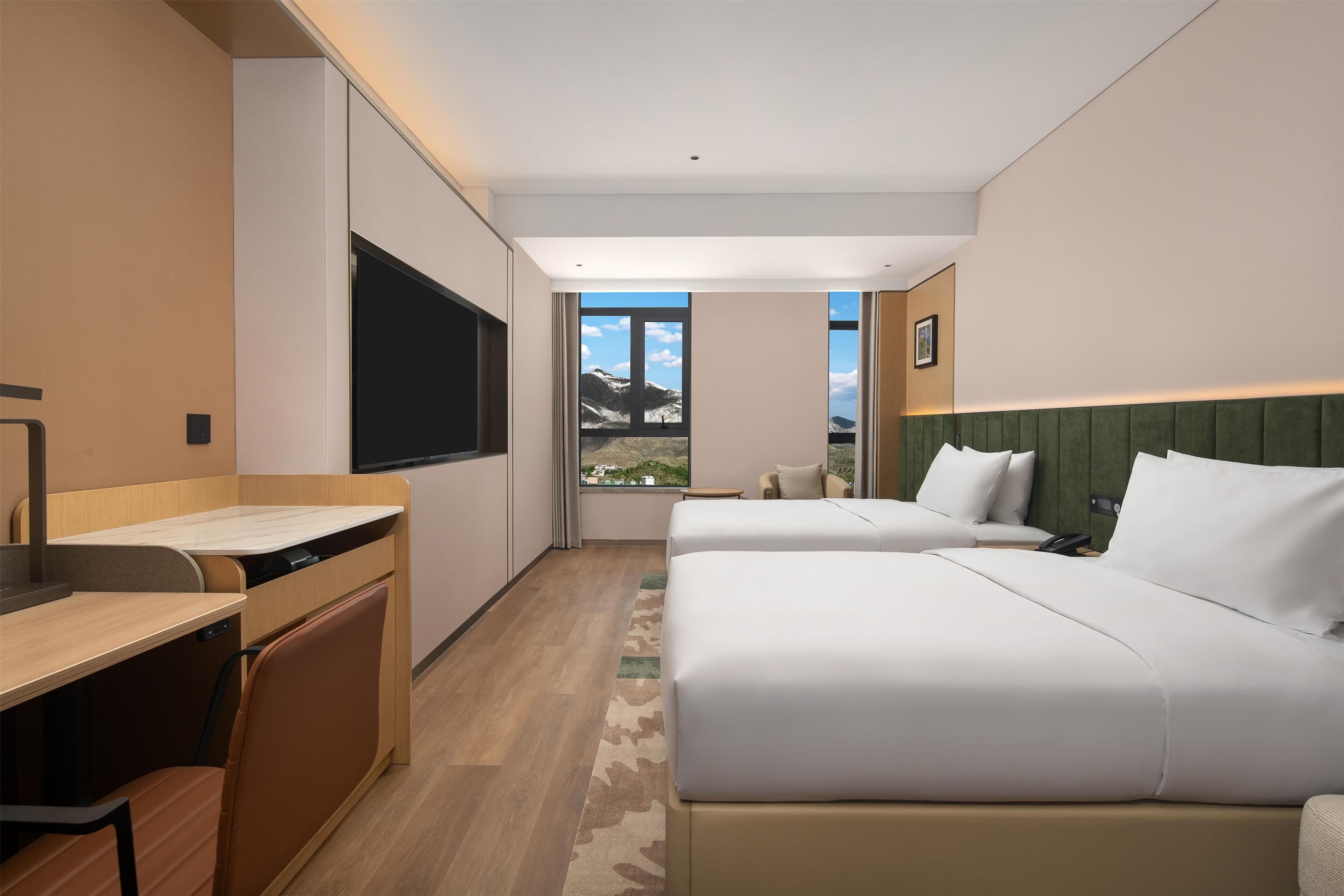 Quarto de hotel com duas camas, uma escrivaninha, uma televisão e vista para montanhas.