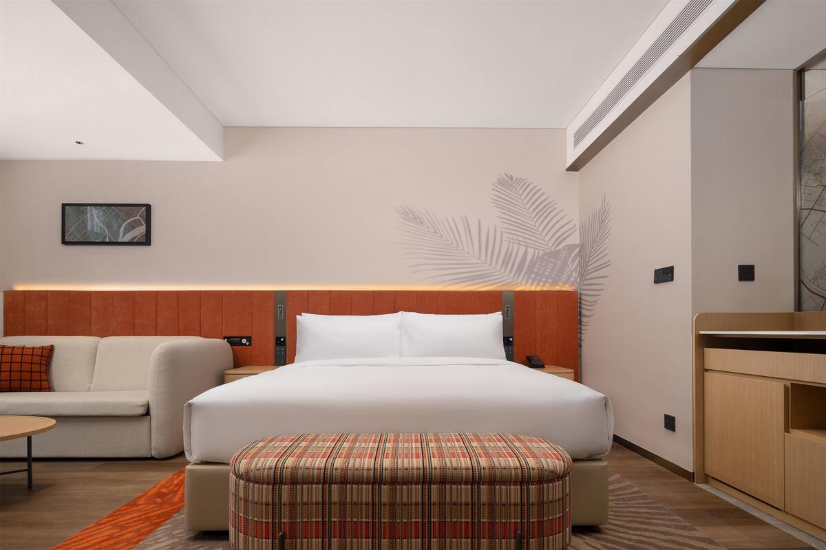Een moderne hotelkamer met een bed, een bank, een kleine tafel en een bankje.