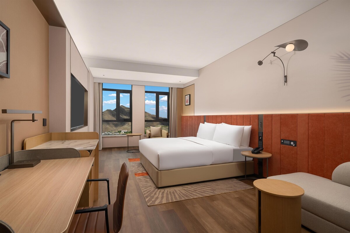 Une chambre d’hôtel moderne dotée d’un grand lit, d’un bureau, d’une chaise, d’une petite table et offrant une vue sur les montagnes.