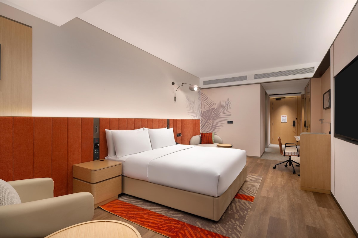 A modern hotel room with a large bed, a desk, a chair, and a TV.
