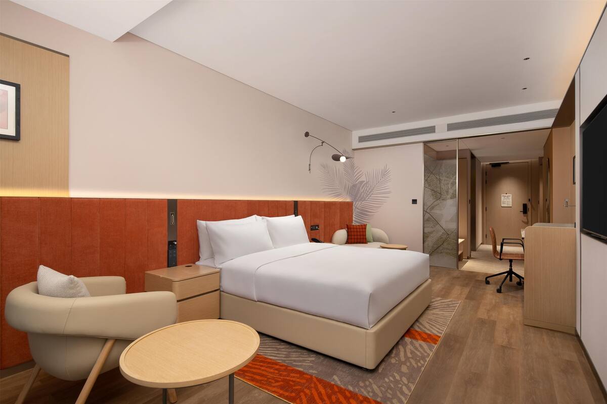 Een moderne hotelkamer met een groot bed, een bureau, een stoel en een bijzettafeltje.