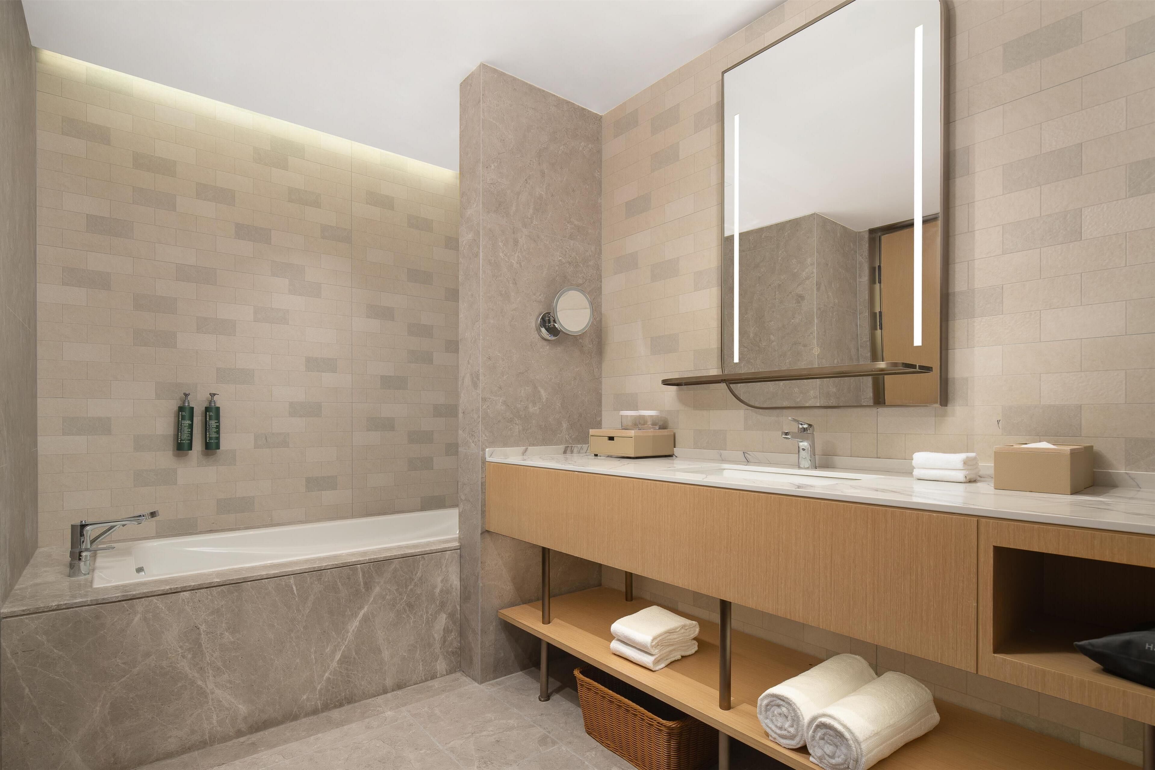 Een moderne badkamer met een bad, een grote spiegel en een wastafelmeubel met een wastafel en handdoekopbergruimte.