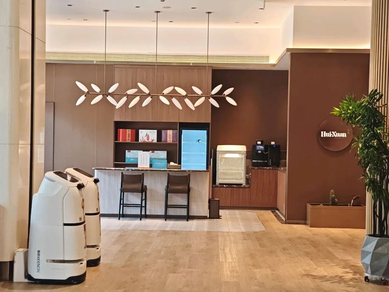 A hotel reception area with a modern design, including a reception desk, seating area, and a large plant.