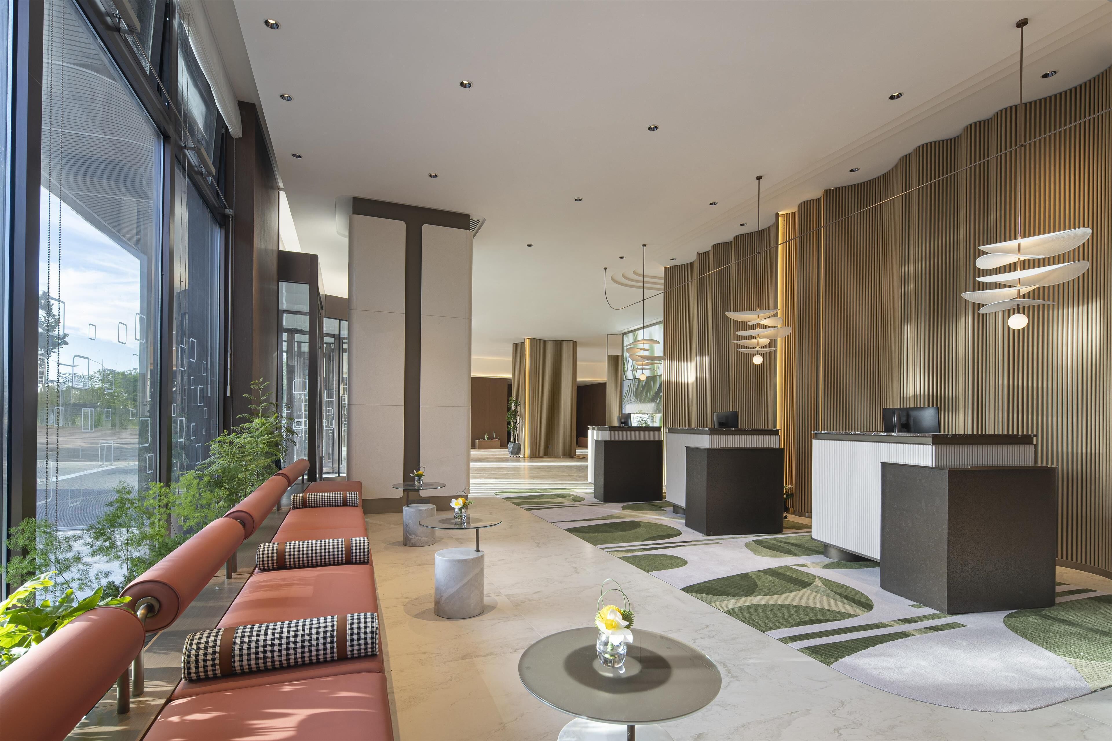 A modern lobby with a reception desk, seating area, and large windows offering a view of the street.