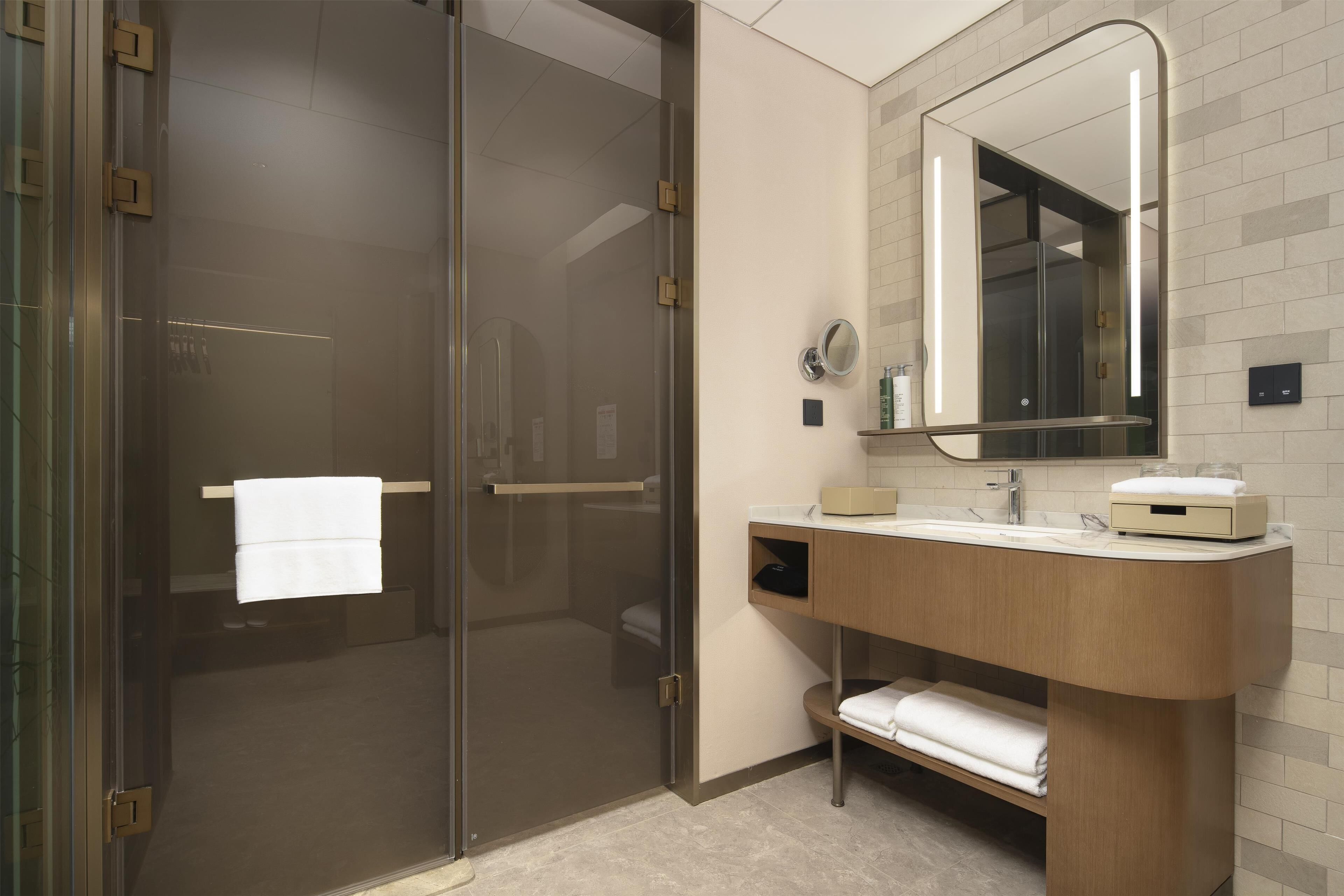 Un baño moderno con cabina de ducha de vidrio, tocador de madera con espejo y perchero.