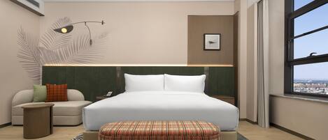 Habitación de hotel moderna con una cama grande, un sofá, una mesita auxiliar y vistas a la ciudad a través de un ventanal.