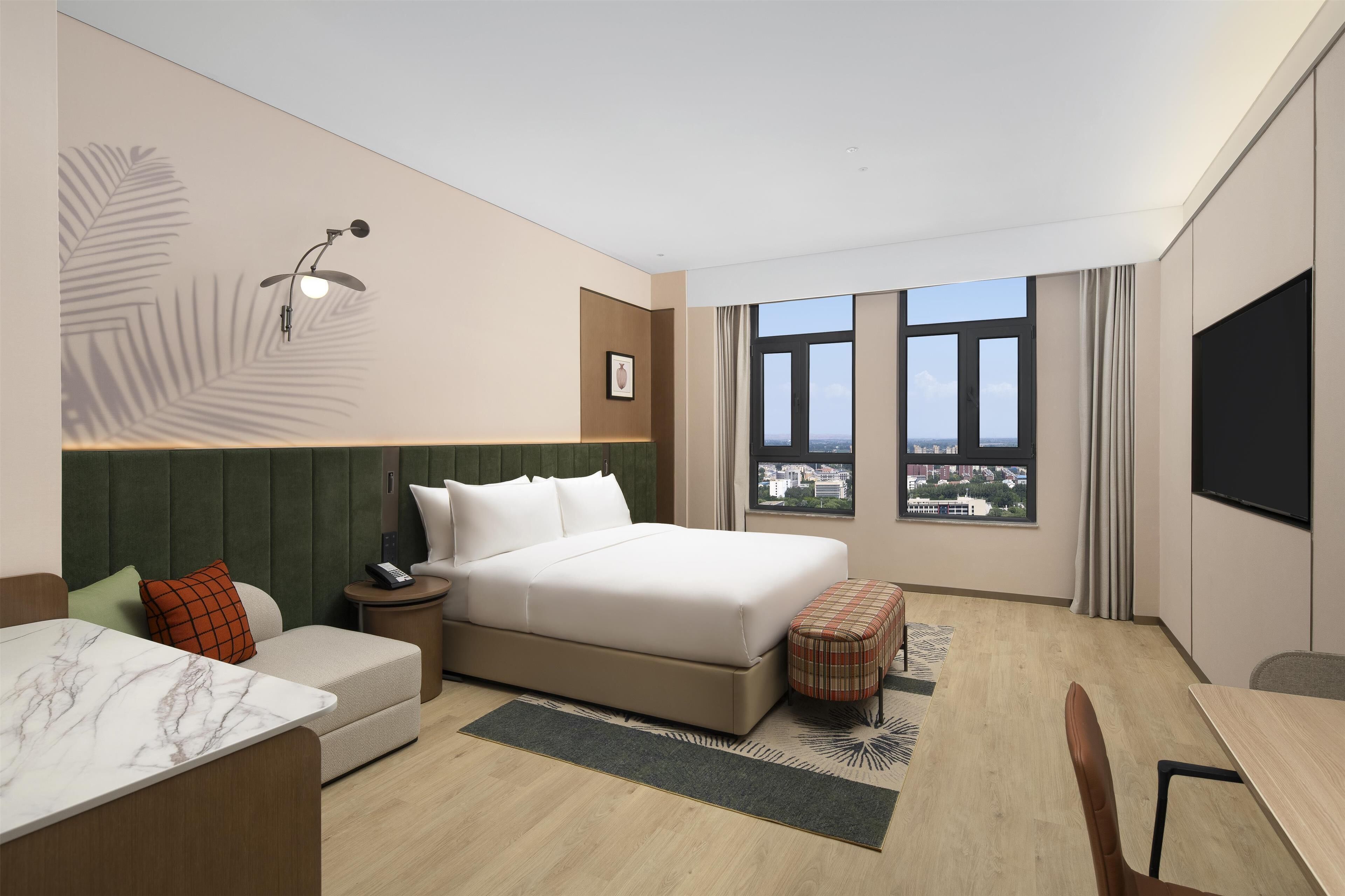 A modern hotel room with a large bed, a sofa, a small table, and a TV.
