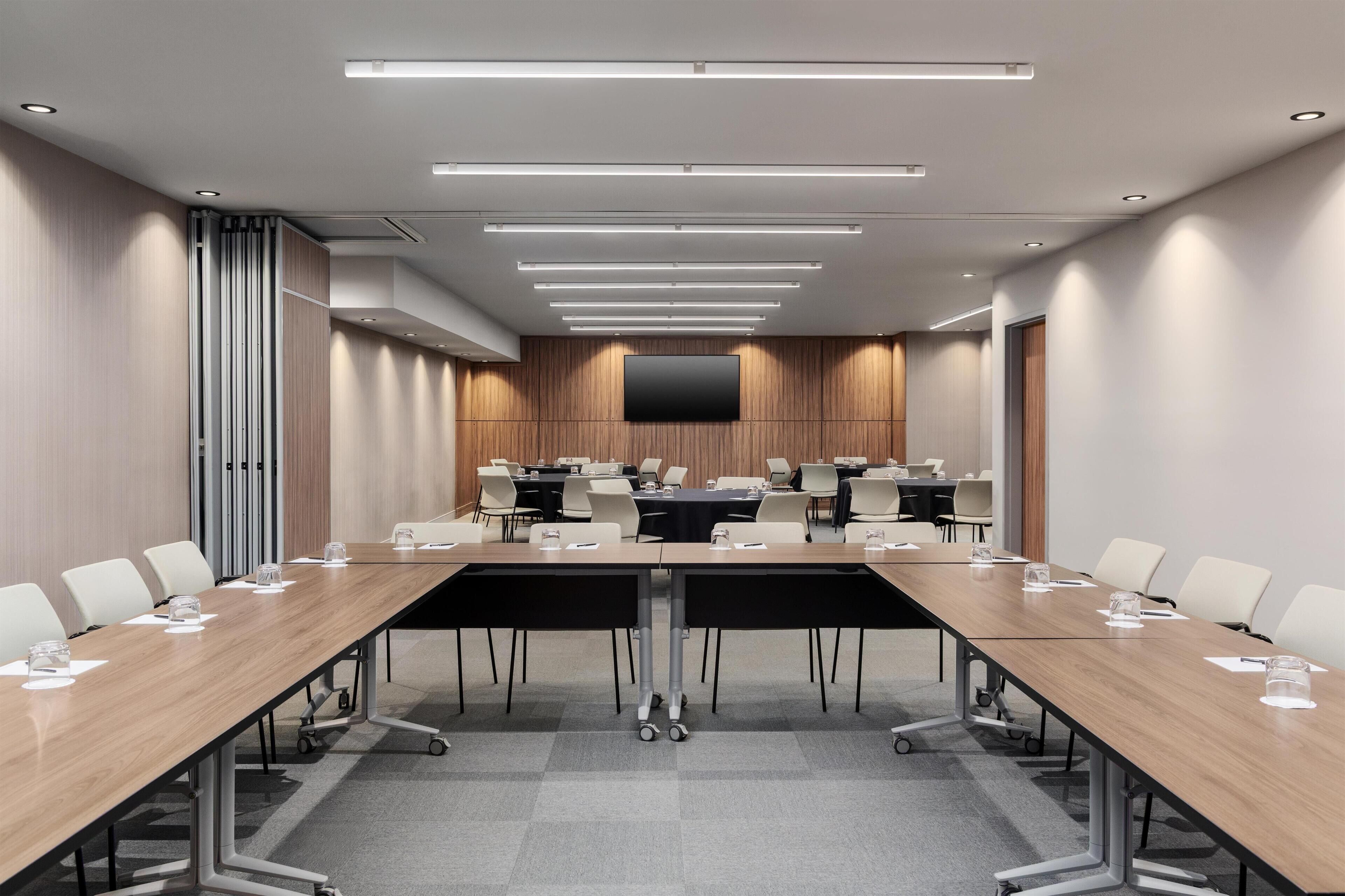 A conference room with a long table, chairs, a flat-screen TV, and ceiling lights.