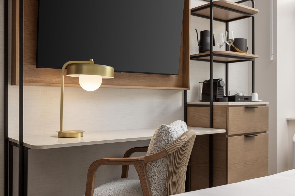 Una habitación moderna con un escritorio de madera, una silla, un televisor montado y una estantería con utensilios de cocina.