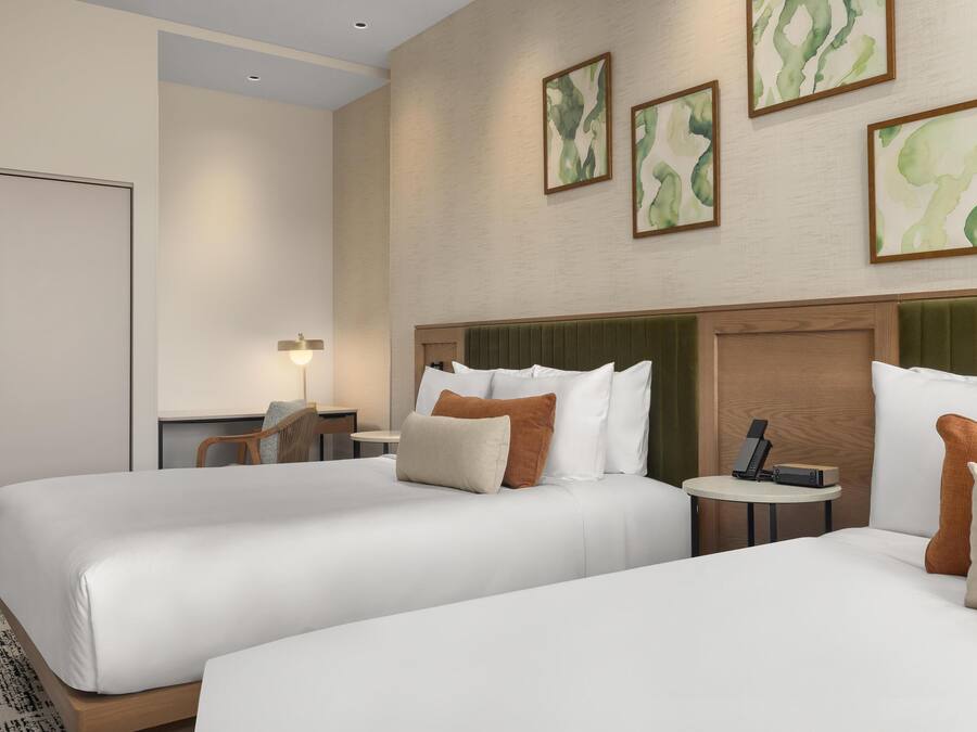 Une chambre d’hôtel avec deux lits, un bureau, une chaise et une petite table sur laquelle se trouvent un téléphone et un appareil de chargement.