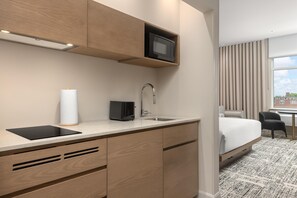 A modern hotel room with a kitchenette, a bed, a desk, and a view of the city. - Hotel Railwayparc Montreal, Tapestry Collection By Hilton (Montreal)