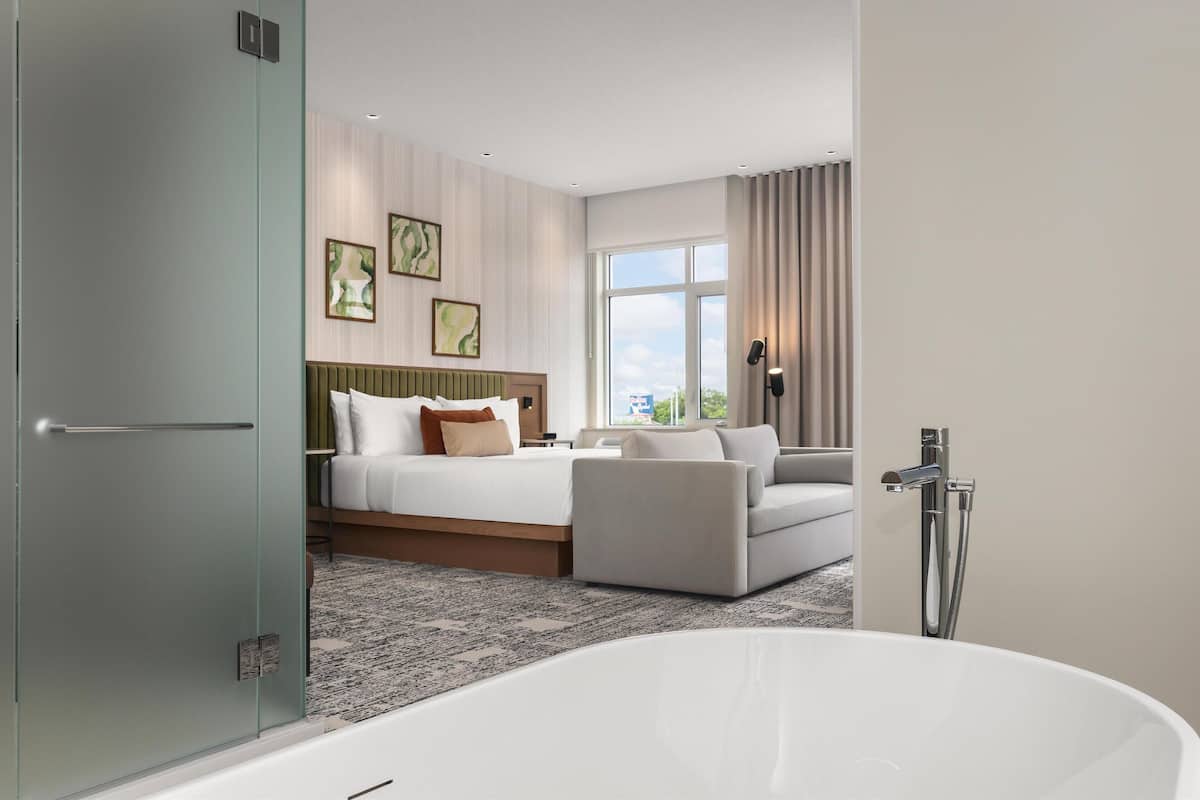 Et moderne hotelværelse med en stor seng, en sofa, et badekar og et stort vindue med gardiner.