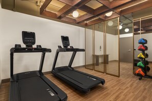 Two treadmills with digital displays, a weight rack with colorful weights, and a wooden floor in a modern room with a glass partition. - Hotel Railwayparc Montreal, Tapestry Collection By Hilton (Montreal)