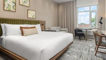 Quarto de hotel com uma cama grande, uma escrivaninha, uma cadeira e uma janela com cortinas.