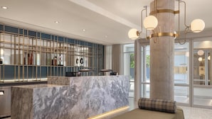 A modern hotel lobby with a marble reception desk, a large pillar, and a seating area. - Hotel Railwayparc Montreal, Tapestry Collection By Hilton (Montreal)