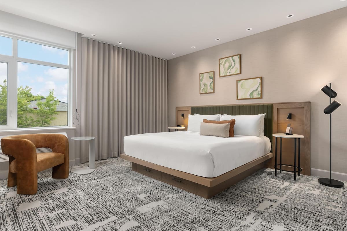 Et moderne hotelværelse med en stor seng, et sengebord, en stol og en gulvlampe.