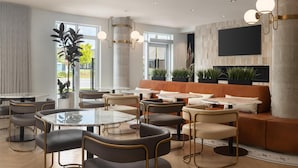 A modern lounge area with round tables, cushioned seating, and a large flat-screen TV mounted on the wall. - Hotel Railwayparc Montreal, Tapestry Collection By Hilton (Montreal)