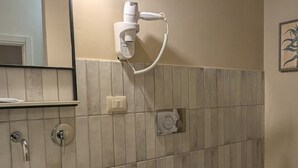 A bathroom with a white sink, a toilet, and a bidet. There is a hairdryer mounted on the wall, a mirror, and a trash can. - Palazzo Russo Ortigia Suite & Apartments (Syracuse)
