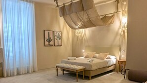 A bedroom with a bed, bench, and a hanging canopy. - Palazzo Russo Ortigia Suite & Apartments (Syracuse)