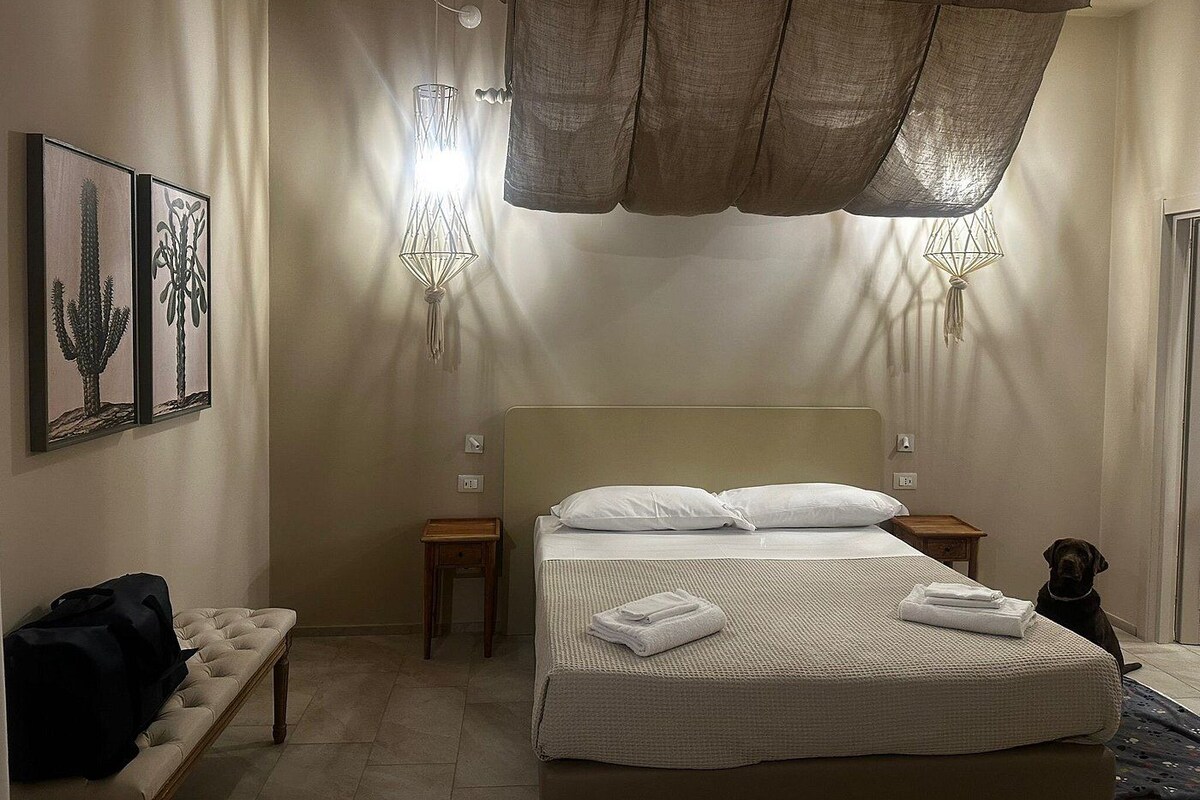 Une chambre d’hôtel avec un lit, des tables de chevet, un banc et des œuvres d’art accrochées au mur.