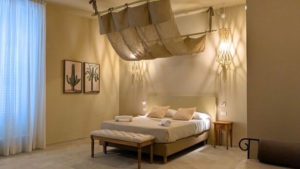A spacious bedroom with a large bed, a hanging canopy, a bedside table, and a nightstand. - Palazzo Russo Ortigia Suite & Apartments (Syracuse)