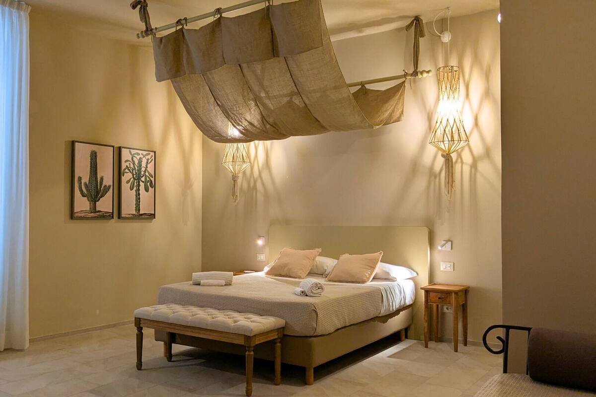Une chambre spacieuse avec un grand lit, un baldaquin suspendu, une table de chevet et une commode.