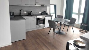 A modern kitchen with grey cabinets, a built-in oven, and a dining area with a round table and chairs. - Exclusive City Apartment Perfect Business Stays (Tuttlingen)