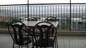 Varanda com mesa e cadeiras, com vista para um horizonte urbano e montanhas.